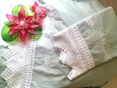 two pieces of white lace on top of a bed next to a red flower and green leaf