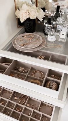 two white drawers with jewelry on them and flowers in vases next to the mirror