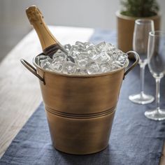 a bottle of champagne in a bucket filled with ice next to two wine glasses on a table