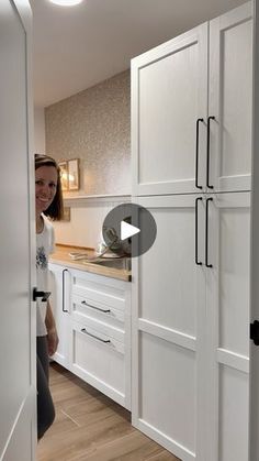 a woman standing in a kitchen next to white cabinets