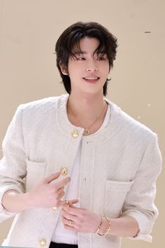 the young man is wearing a white cardigan and black pants with gold rings on his fingers