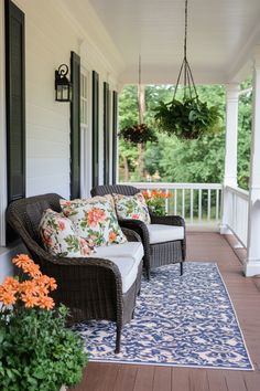 two wicker chairs sitting on a porch with pillows and flowers hanging from the ceiling