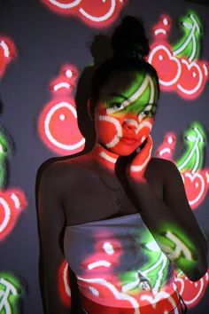 a woman with green and red makeup is talking on her cell phone in front of a colorful background