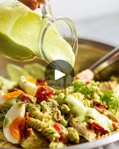 a person pouring dressing into a bowl filled with vegetables and meats to make an avocado salad