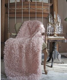 a pink blanket sitting on top of a chair next to a chandelier