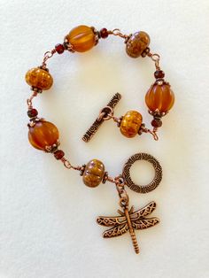 a bracelet with beads and charms on it, including a dragonfly brooche charm