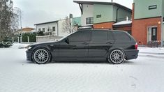 a black car parked on the side of a snow covered road in front of a house