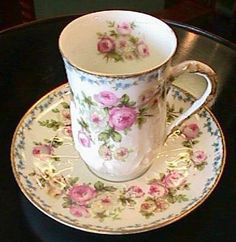 a cup and saucer with pink flowers on it sitting on a black table top