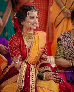 a woman sitting on the ground wearing a red and yellow sari with gold jewelry