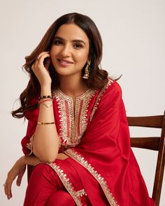 a woman sitting in a chair with her hand on her head and wearing a red dress