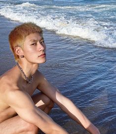 a young man sitting on the beach next to the ocean