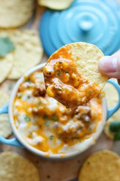 a hand holding a tortilla chip over a bowl of salsa and cheese dip