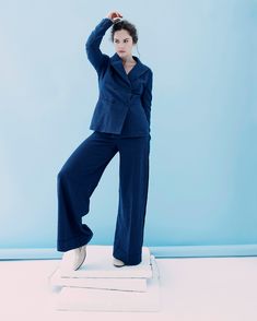 a woman in a blue suit is standing on a white platform with her hands behind her head