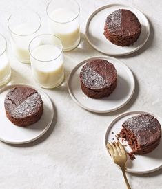 four plates with cakes on them next to glasses of milk