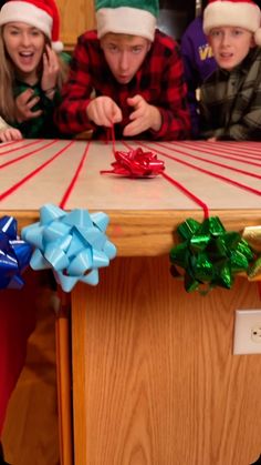 a group of people wearing christmas hats around a table with presents and ribbons on it