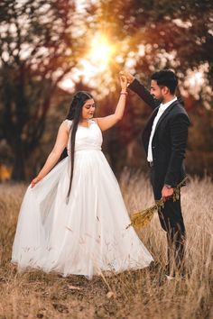 a bride and groom holding hands in a field with the sun shining through the trees