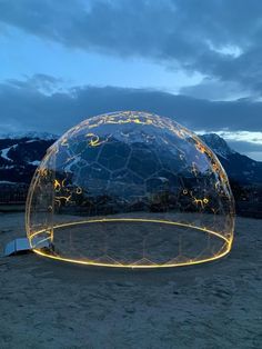 a large glass dome with lights inside on the ground in front of mountains and sky