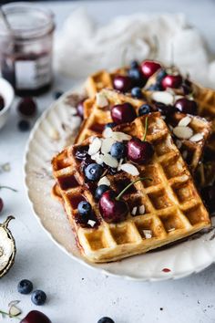 two waffles topped with blueberries and almonds on a plate next to some fruit