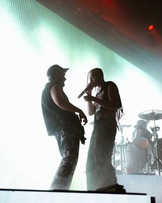 two people on stage with one holding a microphone and the other looking at another person