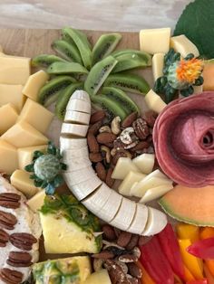 a variety of cheeses and fruits are arranged on a cutting board with green leaves