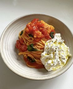 a white bowl filled with pasta, sauce and vegetables on top of a table next to a fork