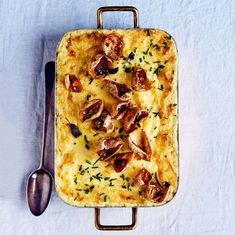 a square casserole with mushrooms and herbs on it, next to a spoon