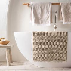 a white bath tub sitting next to a wooden stool and towel rack in a bathroom