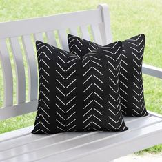 two black and white pillows sitting on top of a white bench in front of grass