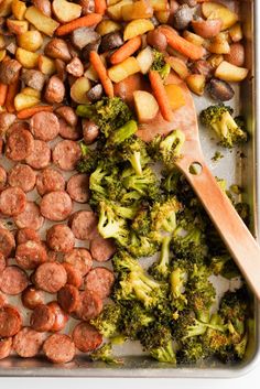 sausage, broccoli and potatoes on a baking sheet with a wooden spoon in it