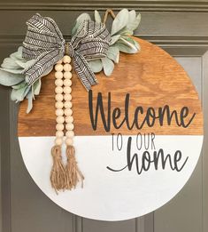 a welcome to our home sign hanging on the front door with wood beads and tassels