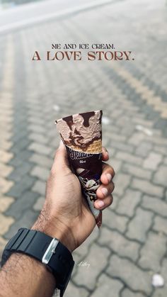 a hand holding up an ice cream bar in front of a cobblestone road