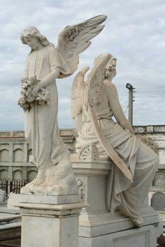 two angel statues sitting next to each other on top of a cement slab in front of a building