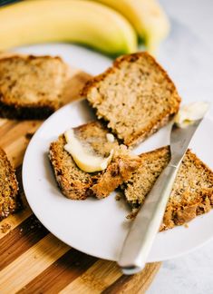 slices of banana bread on a white plate with a knife and bananas in the background