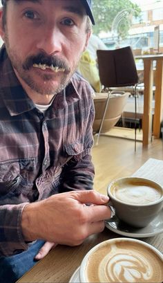 a man sitting at a table with two cups of coffee