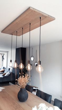 a dining room table with several lights hanging from it's ceiling and flowers in the center