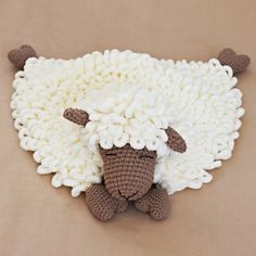 a crocheted sheep laying on top of a brown and white blanket