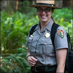 a woman police officer standing in the woods with her back pack and smiling at the camera