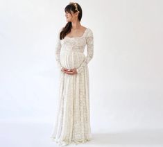 a pregnant woman wearing a white dress with long sleeves and a lace overlay, standing in front of a white background