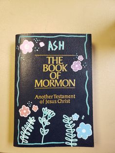 the book of mormon with flowers and leaves on black leather cover hanging from a wall