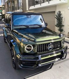 a green mercedes g - class parked in front of a building