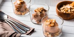 three glasses filled with ice cream and nuts on top of a white tablecloth next to silverware