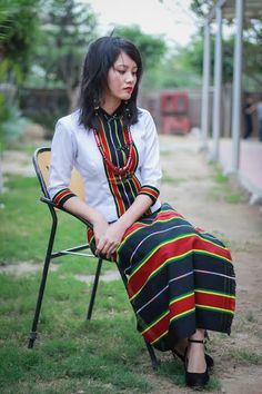 a woman is sitting on a chair in the grass wearing a colorful dress and necklace