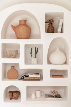 shelves with vases, books and other items on top of them in a white room