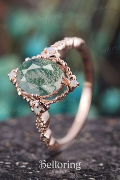 a close up view of a ring with green stone in the center and diamond accents