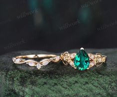 two rings with green and white stones on them sitting on top of a mossy rock