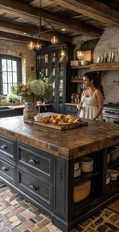 a woman standing in a kitchen next to an island with fruit on it and plates