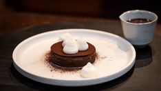 a chocolate dessert with marshmallows on a white plate next to a cup of coffee