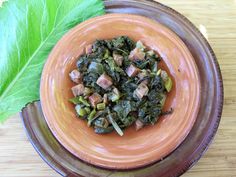 a bowl filled with greens and meat on top of a wooden table next to a leaf