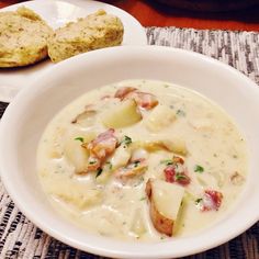 a white bowl filled with soup next to a piece of biscuit on a table