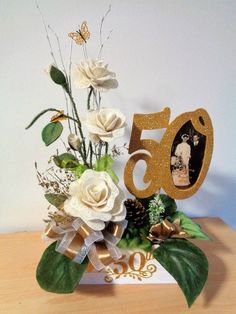 a 50th birthday card with white flowers and greenery on a wooden table next to a pine cone